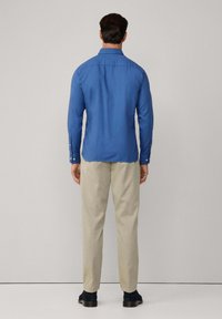 Blauwe overhemd met lange mouwen en kraag, met geknoopte manchetten en een rechte snit. Gepaard met lichtbeige broeken en donkere schoenen.