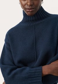 Marineblauwe coltrui van ribbelstof, met een hoge kraag en brede mouwen, in een oversized stijl.