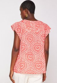 Blusa a maniche a soffietto rossa e bianca con motivo paisley; caratterizzata da intricate spirali e un tessuto morbido e leggero.