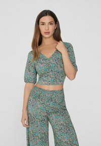 Zelený květinový crop top s krátkými nabíranými rukávy a výstřihem do V, spárovaný s odpovídajícími širokými kalhotami s podobným vzorem a elastickým pasem.