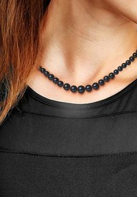 Collier de perles noires avec des perles de taille variable, texture lisse et design uniforme, reposant sur le décolleté contre une chemise noire.