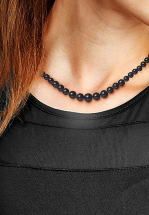 Collier de perles noires avec des perles de taille variable, texture lisse et design uniforme, reposant sur le décolleté contre une chemise noire.