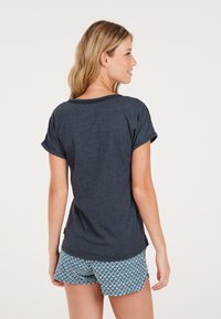 T-shirt navy a maniche corte con orli arrotolati, texture morbida e vestibilità rilassata, abbinato a pantaloni corti blu con motivi floreali.