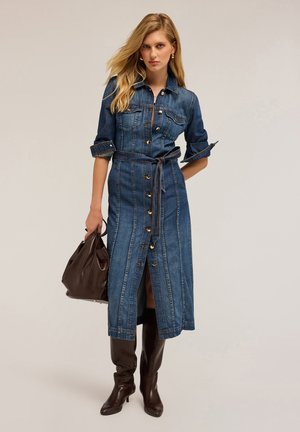 Abito camicia di denim blu scuro con bottone frontale, maniche lunghe e cintura. Abbinato a stivali in pelle marrone alti fino alla coscia e una borsa marrone.