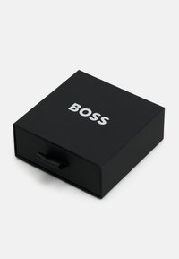 Crna kartonska kutija s povlačnom kopčom, na gornjoj površini s natpisom "BOSS" u bijelim velikim slovima. Glatka tekstura i minimalistički dizajn.