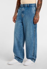 Light blue denim wide-leg jeans with a high waist, featuring front pockets and subtle fading; worn with white sneakers.