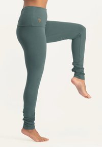 Hochtaillierte, petrolfarbene Yoga-Leggings aus weichem, dehnbarem Stoff. Verfügt über einen gerafften Bund und angeschnittene Fußöffnungen. Besticktes Logodetail.