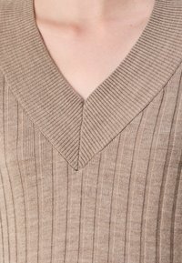 Beige bordás kötött pulóver mély V-nyakkivágással és texturált felülettel, függőleges vonalakkal és puha megjelenéssel.