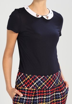 Camiseta azul marino de manga corta, con cuello Peter Pan blanco decorado con adornos coloridos, combinada con pantalones estampados multicolores.