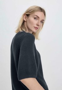 Yli suuri tummanharmaa neulepaita lyhyillä hihoilla, ribbitekstuuri ja väljä istuvuus, joka esittelee rentoa ja huoleton tyyliä.