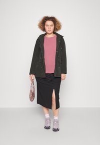 Parka nera con cappuccio e cordini, top rosa, gonna nera a coste con spacchi, sneakers sportive grigie e borsa stampata.