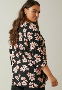 Blusa nera con motivo floreale bianco e rosso, maniche a tre quarti, vestibilità morbida, tessuto liscio e orlo arrotondato.