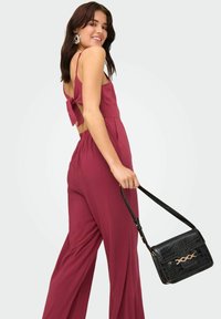 Combinaison bordeaux avec une conception à nouer dans le dos, dotée d'une coupe ample et de jambes larges. Sac à main noir en cuir crocodile avec des accessoires en or.