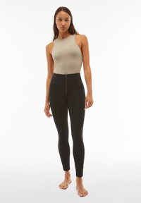 Leggings neri a vita alta con cerniera frontale, abbinati a un top aderente beige. Tessuto liscio senza motivi visibili.