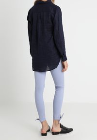 Marine linnen overhemd met lange mouwen en rugdetails, gecombineerd met lichtblauwe slim-fit broeken met zijstrikaccenten en zwarte instapschoenen.