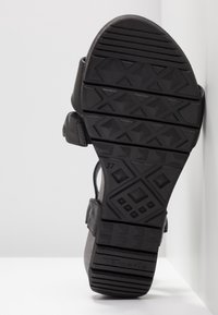 Sandale noire avec une semelle en caoutchouc texturée, présentant des motifs géométriques et des sangles réglables. Taille 37 indiquée sur la semelle intérieure.