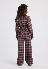 Plaid two-piece set in burgundy, featuring a tie-back blouse with long sleeves and wide-leg pants. Smooth fabric with a checkered pattern.