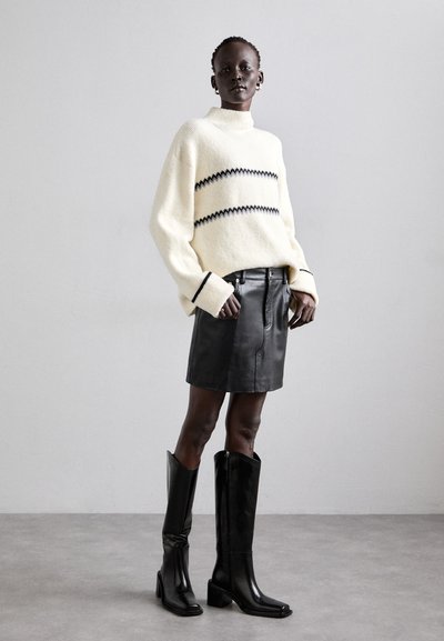 Cream knitted sweater with black stripes, paired with a black leather mini skirt and tall black heeled boots, showcasing a sleek silhouette.