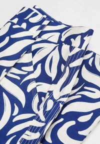 Close-up van blauwe en witte stoffen met een patroon van abstracte bladvormige vormen en zichtbare naden en steken.