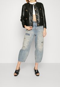 Černá kožená bunda se čtyřmi předními kapsami a zlatými knoflíky, v kombinaci se sepranými světle modrými džíny a černými sandály na podpatku.