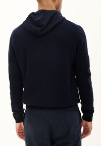 Granatowy sweter z kapturem wykonany z miękkiego materiału, z przewiewnym krojem i ściągaczami przy mankietach. Gładka faktura bez widocznych wzorów czy akcentów.
