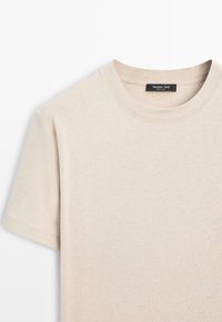 T-shirt in cotone beige con collo rotondo e maniche corte. Texture liscia, design minimale. Etichetta visibile al collo.