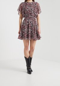 Robe courte évasée en tissu transparent avec un motif abstrait coloré, présentant une taille froncée et des manches volantées. Associée à des bottes noires.