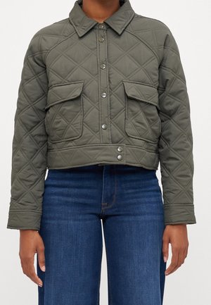 Quiltet olivengrøn cropped jakke med trykknapper og klaplommer, båret med mørkeblå denimjeans.