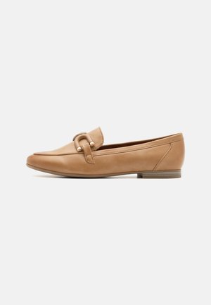 Kohver-kollased nahast loafersid ümarate varvastega, dekoratiivse rihma ja metallaktsentiga. Lamedad tald ja minimaalne õmbluste detail.