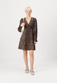 Vestido envolvente com estampa de leopardo, mangas longas, decote em V profundo e acabamento preto. Modelo segura uma bolsa clara. Sapatos planos com ponta redonda.