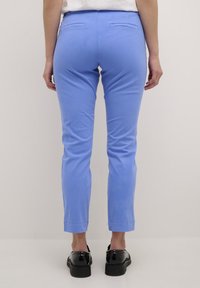 Pantalons ajustés bleu clair avec une texture lisse, dotés de deux poches arrières et d'un design de jambe fuselée, accompagnés de chaussures noires.