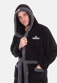 Zwarte pluchen ochtendjas met grijze accenten, kap en riem. Bevat "THE PUNISHER" geborduurd in het wit op de voorkant. Zacht, textuurmateriaal.
