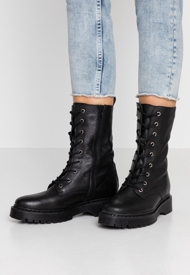 Svarta läderankelboots med snörning framtill, dragkedja, rund tå och texturerad yta. Tjock gummisula med mönstrade spår.