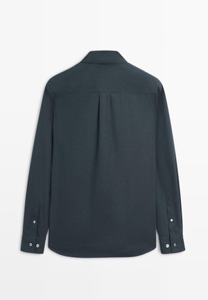 Mørkegrå langærmet skjorte med knappede manchetter, spids krave og central læg bagpå, vist bagfra på en hvid baggrund.