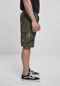 Bermudas de camuflaje en tonos verdes con un diseño de múltiples bolsillos. Fabricadas con tela duradera, presentan un corte relajado y se combinan con zapatillas negras.