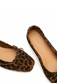 Paire de ballerines en daim à imprimé léopard avec bouts arrondis et petit détail nœud sur fond blanc.