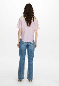 Chemise courte à manches courtes de couleur rose clair avec une texture rayée et un accent jaune sur les épaules, associée à un jean flare bleu taille haute.