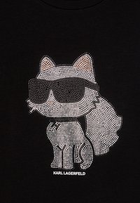 T-shirt preta com um design de gato feito de strass prateados, usando óculos de sol, com o texto "KARL LAGERFELD" na parte inferior.