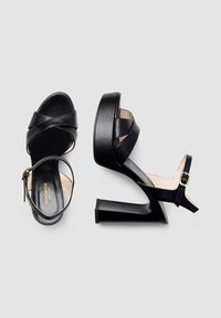 Sandali neri con tacco alto, con cinghie incrociate, design con punta aperta, finitura in pelle liscia, suola a piattaforma e cinturino alla caviglia con fibbia.