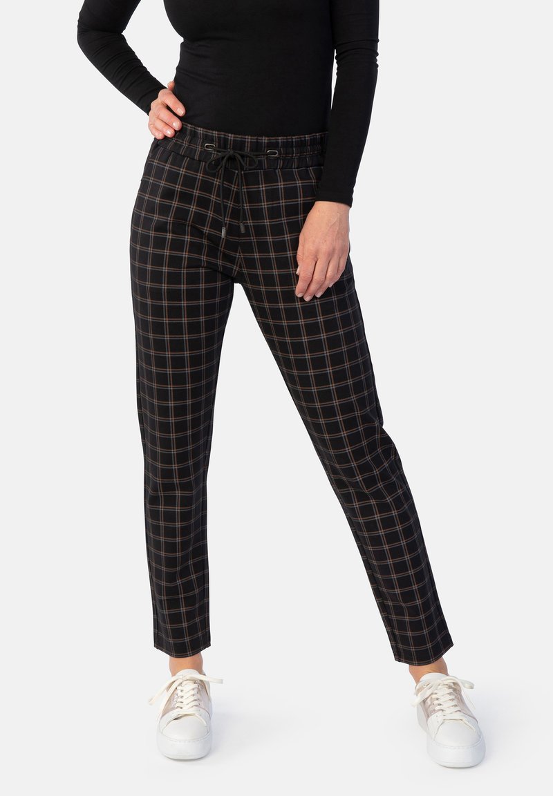 Schwarze und karierte tapered Pants mit elastischem Bund und Kordelzug. Kombiniert mit einem enganliegenden schwarzen Langarmoberteil und weißen Sneakers.