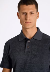 Tummanharmaa poolopaita, joka on valmistettu teksturoidusta kankaasta, ja siinä on kaulus, kolme ruskeaa nappia ja lyhyet hihat.