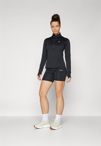 Black long-sleeve athletic top with a half-zip collar, paired with black shorts. Textured fabric, fitted design, and light-colored sneakers.