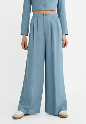 Lyseblå bukser med høj talje og brede ben, båret med en matchende cropped jakke og hvide sneakers.