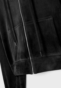 Sweat à capuche noir zippé avec poches avant et cordons noirs sur un tissu doux, présenté en gros plan.