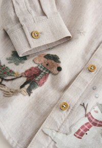 Beige Hemd mit Knöpfen und Fischgrätmuster, das eine Abbildung von einem Reh und einem Schneemann zeigt. Goldene Knöpfe und weicher Stoff.
