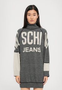 Lielizmēra augsta apkakle pelēkā krāsā ar kontrastējošajām gaiši pelēkajām piedurknēm. Priekšpusē ir izteiksmīgi uzraksti "SCHI" un "JEANS" krēmkrāsā.