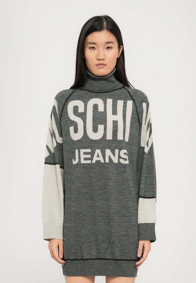 Maglione oversize a collo alto di colore grigio scuro con maniche di un grigio chiaro a contrasto. Presenta una scritta audace "SCHI" e "JEANS" in crema sul davanti.