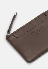 Brązowy skórzany portfel z zamknięciem na zamek, teksturowaną powierzchnią, przeszywanymi krawędziami i wytłoczonym logo marki. Posiada pasek na nadgarstek do przenoszenia.