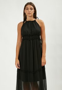 Vestido negro halter confeccionado en una tela ligera, con cintura fruncida, falda en capas que fluye y acentos con volantes a lo largo del dobladillo.