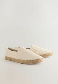 Beige slip-on sko med en tekstureret stofoverdel, elastiske detaljer og en flettet jutesål. Letvægts- og afslappet design.
